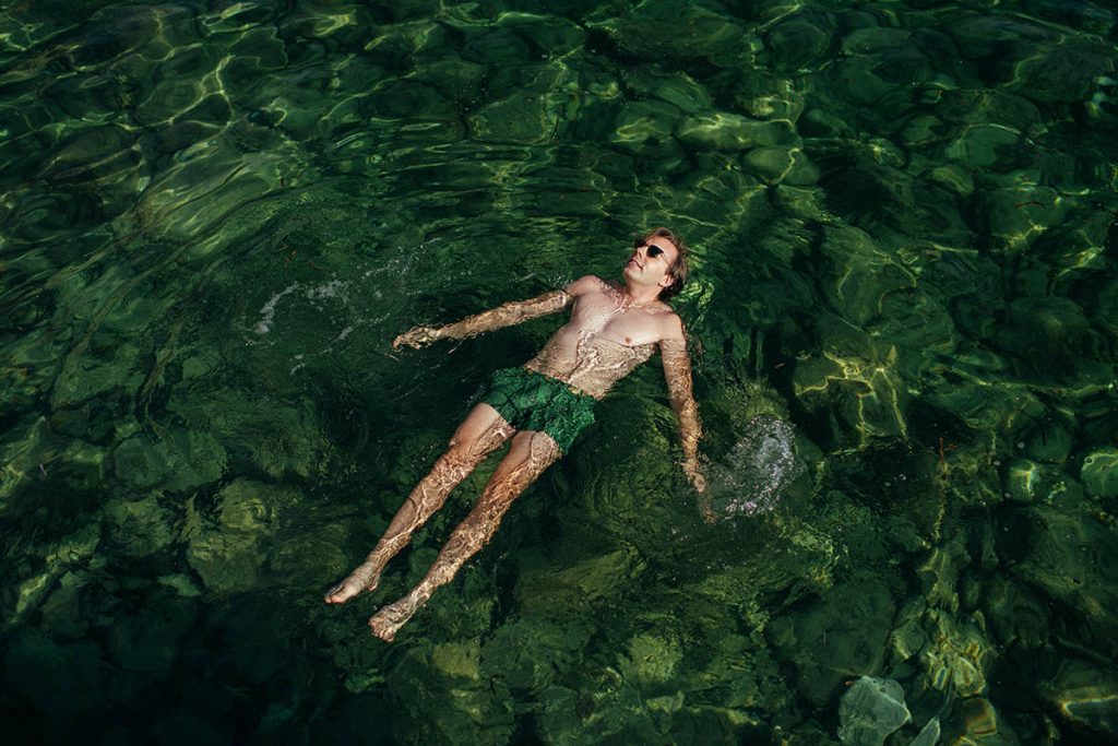 A man floating in the water while wearing floating sunglasses, enjoying a sunny day near the ocean.