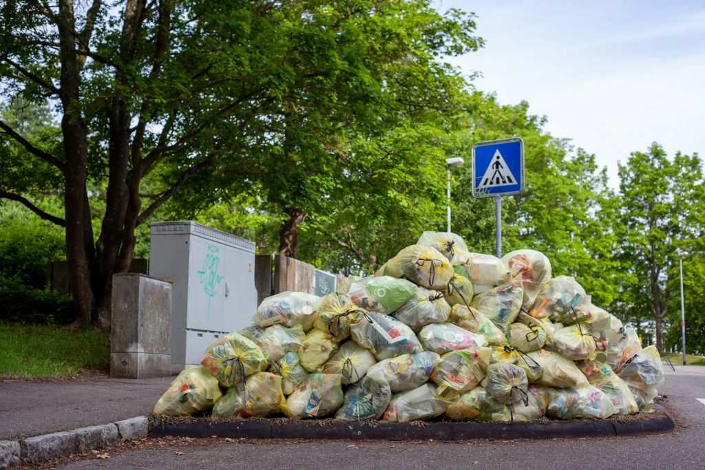 A cluttered pile of black garbage bags and loose rubbish stacked on a street corner, creating an untidy and unpleasant environment.