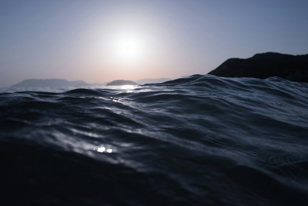 A tranquil scene of the sea with gentle waves rolling under a clear sky, reflecting hues of blue and turquoise. The horizon seamlessly blends into the vast expanse of water, evoking a sense of calm and serenity.