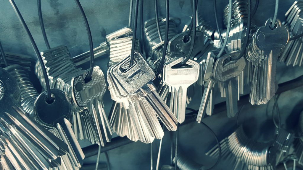 A close-up view of multiple sets of metal keys hanging on wire loops, organized in a locksmith's workshop. The keys have various shapes and designs, reflecting light off their metallic surfaces.