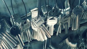 A close-up view of multiple sets of metal keys hanging on wire loops, organized in a locksmith's workshop. The keys have various shapes and designs, reflecting light off their metallic surfaces.