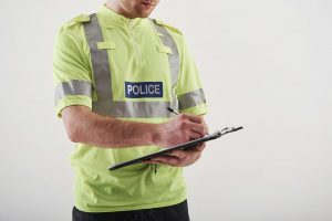 Police officer issuing a penalty notice on a clipboard, representing someone being caught driving without insurance in the UK.