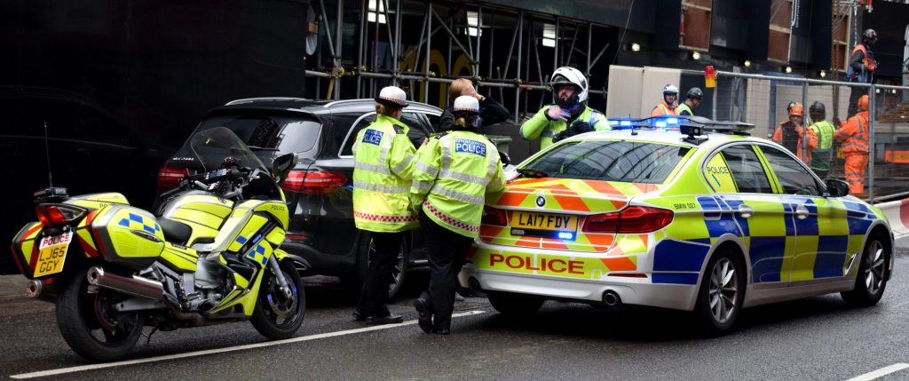 Cardiff Police officers and vehicles at a street scene near a construction site, addressing a potential motoring offence.