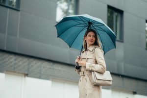 Woman walking in the rain holding a stylish umbrella, representing everyday use of custom umbrellas.
