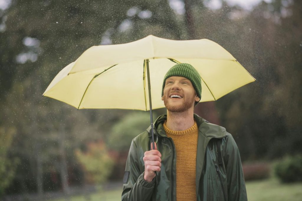 Man smiling under a yellow umbrella in the rain, showcasing the use of promotional umbrellas outdoors.