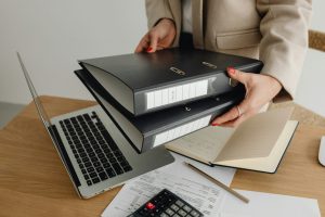 woman placing two binders on the table next to her laptop