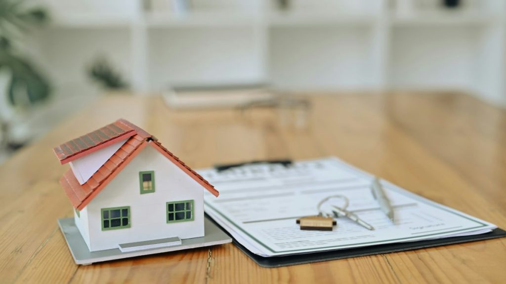 Mortgage brokers Cardiff concept showing miniature house model beside mortgage paperwork and house keys on a wooden table.